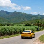 Coche amarillo moderno saliendo de Trinidad, con las montañas del Escambray al fondo